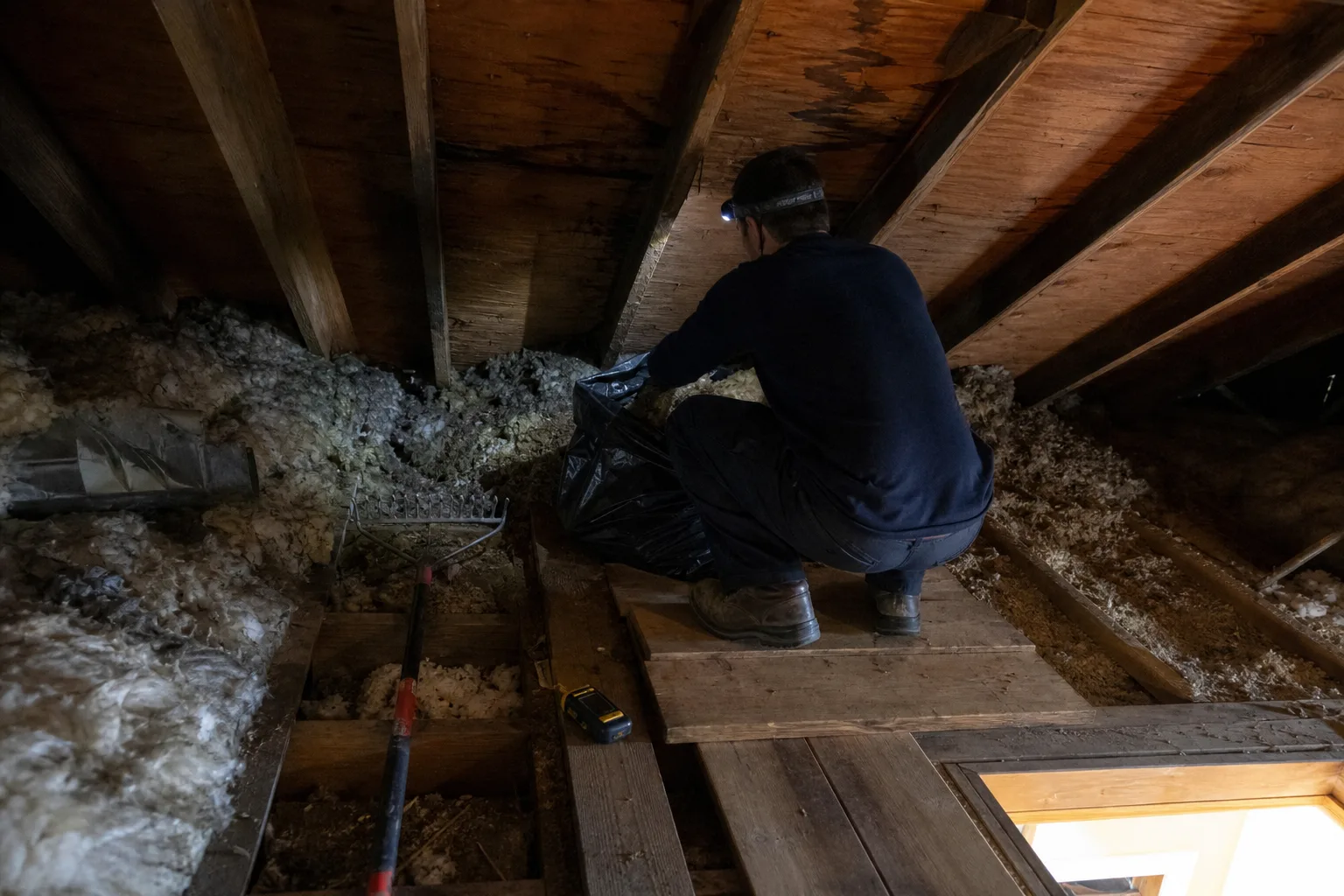 A technician removing wet attic insulation beneath a stained roof deck - for Roof Leak Water Damage in Chula Vista, CA
